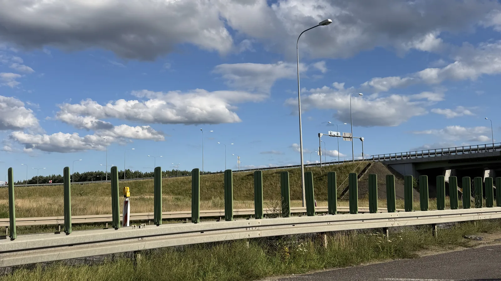 Ekran akustyczny wzdłuż trasy przy wschodniej granicy gminy Białe Błota — zielone panele za barierą energochłonną, w tle estakada