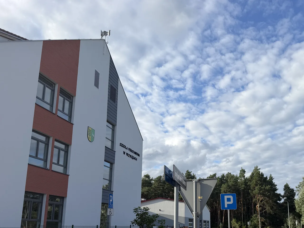 Szkoła Podstawowa w Przyłękach — trzykondygnacyjny budynek z białą i ceglaną elewacją, herb gminy Białe Błota